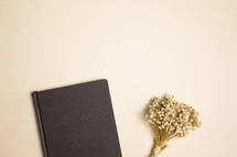 Black notebook and dried flowers on tan background
