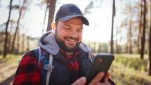 Young attractive man during the hike hold mobile phone, share message to friend distantly use social media network, watch received video, fun online concept. Technology and adventure concept.