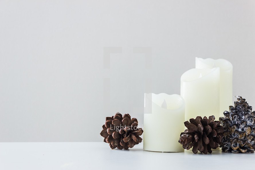 three white candles and pine cones 