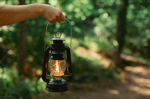 A hand hold an oil lantern in a trail. 
