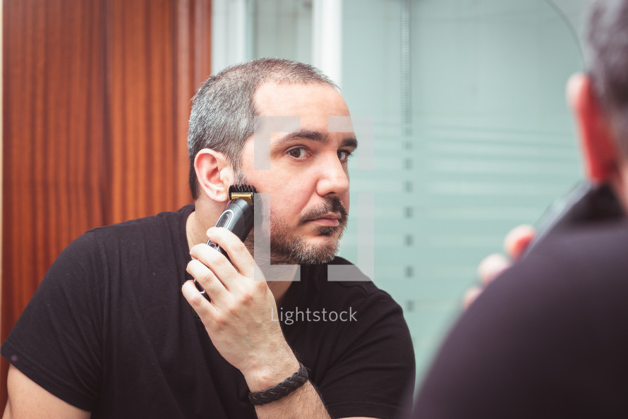 bearded man trimming his beard with a trimmer
