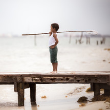 a boy holding a fishing net standing on a dock 