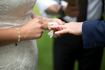 A bride placing a ring on the groom's finger during a wedding ceremony.