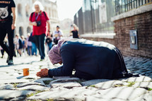 a beggar kneeling on a cobblestone street 