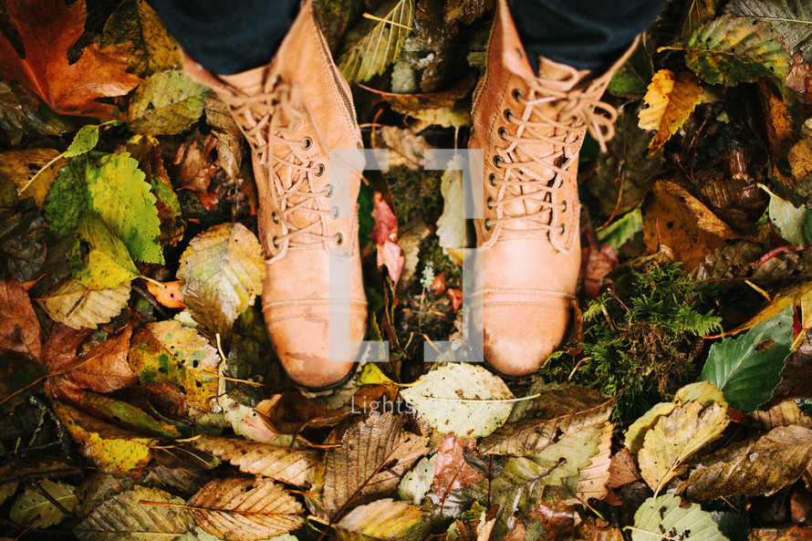 A person standing in boots surrounded by autumn leaves