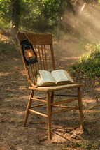 A Bible and oil lantern on a chair in the woods.