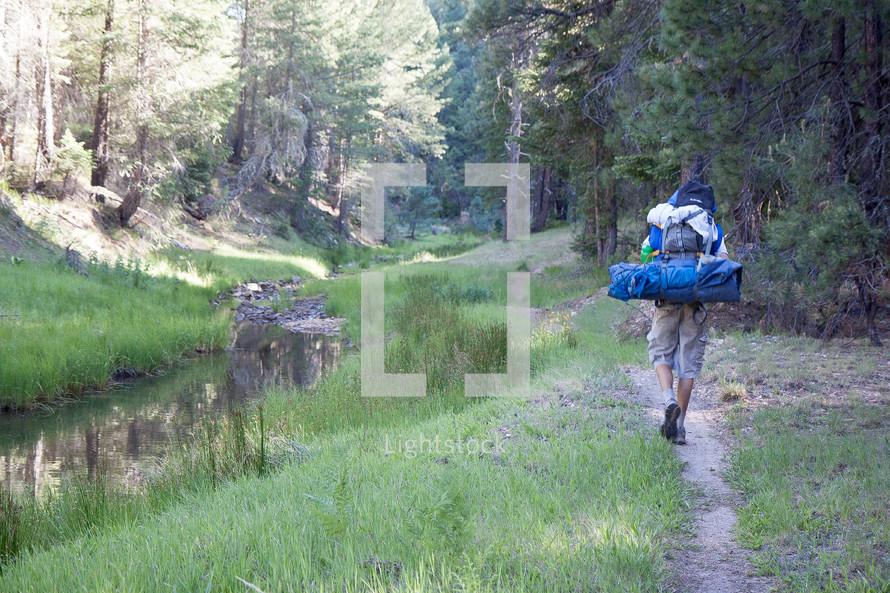 hiker with camping gear on his back walking on a trail 