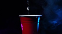 Pouring beer into a red solo cup with party lights and smoke