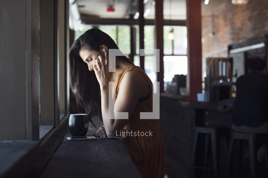 a young woman sitting in front of a window in a coffee shop listening to earbuds 