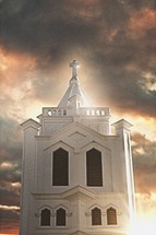 sunlight shining through a cloudy sky on a white church steeple