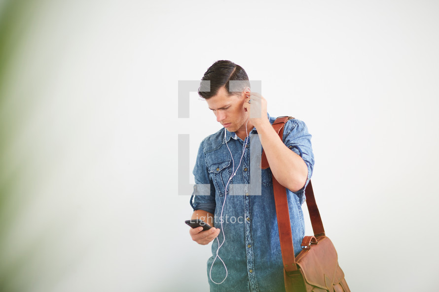 a man standing holding a messenger bag listening to earbuds