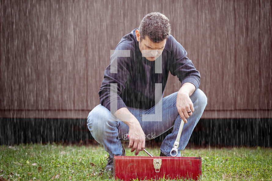 a man standing outdoors going through a red toolbox in the rain 