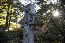 Stone cross surrounded by trees and plants