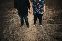 a couple standing in a field of dry grass holding hands 