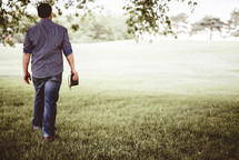a man walking through a field carrying a Bible 