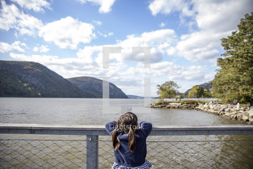 Little girl with pigtails on a fence in front of water