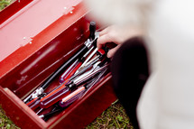 a woman sorting through a red toolbox full of tools 