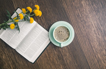 yellow flowers, opened Bible, and coffee cup on a wood table 
