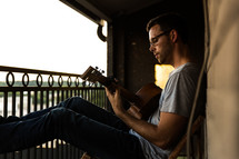 man playing a guitar on a balcony 