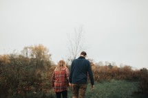 a couple walking through a field holding hands 