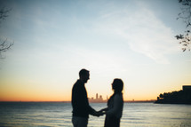 a couple holding hands with a city skyline in distance across the water 