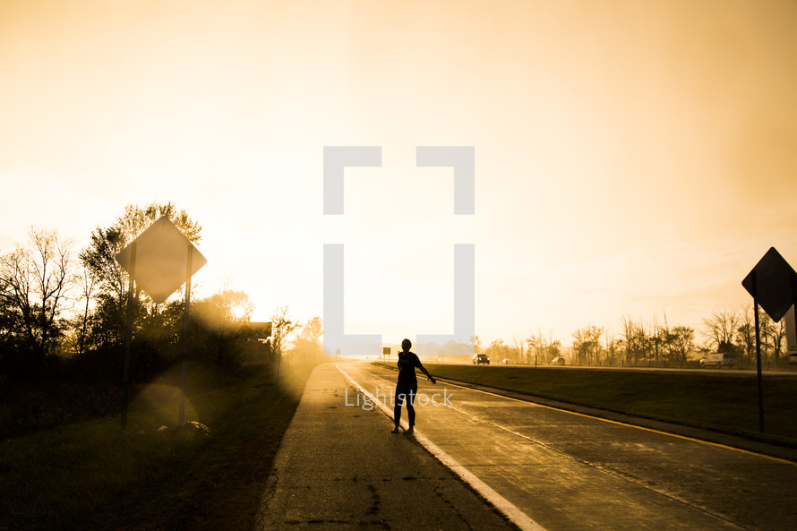 a silhouette of a woman standing on the side of a road 
