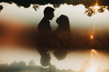 silhouette of a couple standing near a lake at sunset 
