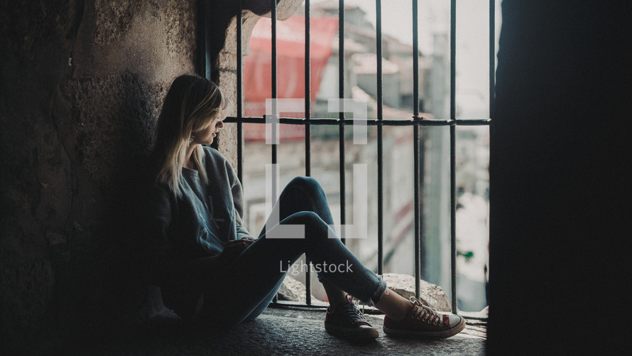 woman sitting in a window with bars 