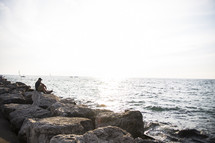 a man sitting on a rock relaxing by the ocean 
