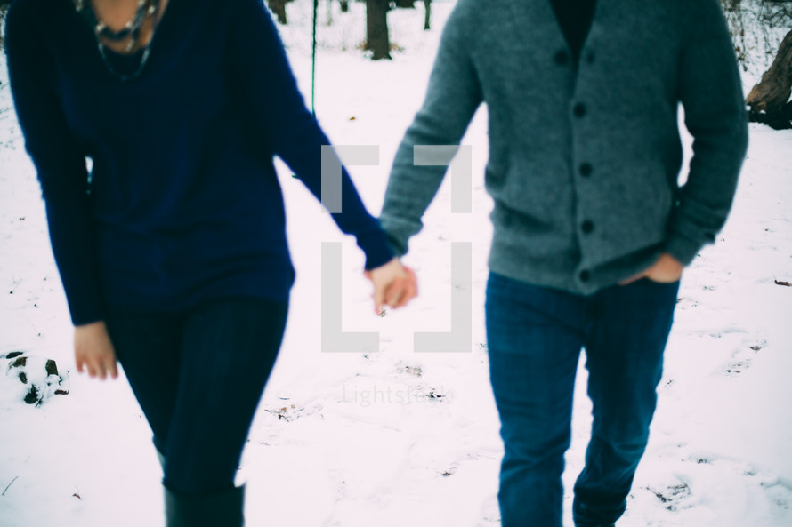 couple holding hands walking through snow 