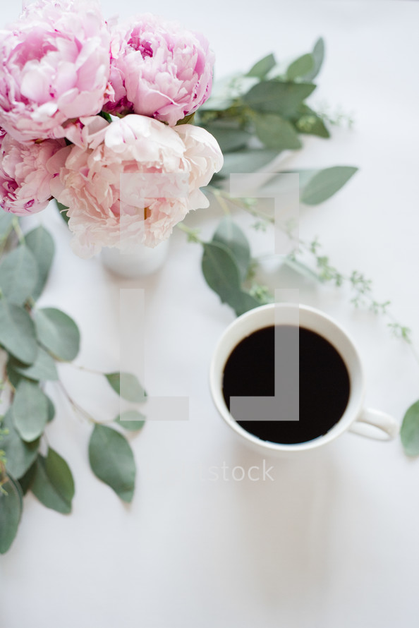 pink peonies in a vase and leaves on a desk with coffee mug 