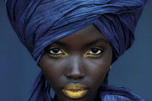Portrait of a woman with denim headwrap and makeup.