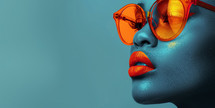Close-up of a woman wearing orange sunglasses with striking blue skin and orange lips.