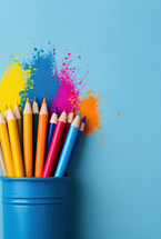 Close-up of colorful pencils in a blue holder with vibrant paint splashes on a matching blue background, symbolizing creativity and artistic expression.