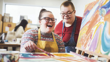 Adult students with Down syndrome enjoying an art class, creating vibrant paintings with laughter.