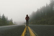 man standing in the middle of a road in fog 