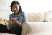 An African American woman sitting on a couch checking her cellphone 
