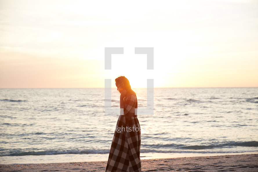 a woman walking on a beach in a dress at sunset 