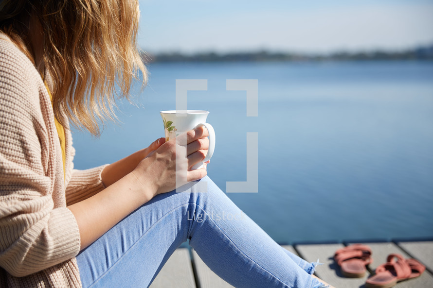 a woman sitting on a pier with a coffee cup 