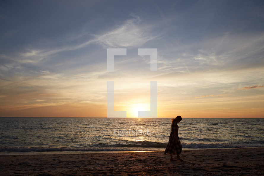 a woman walking on a beach at sunset 