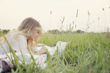 young woman reading on a blanket in the grass 