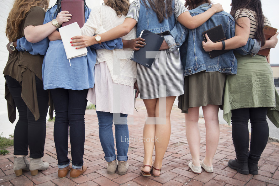 A group of young women with their arms around each other and holding Bibles.