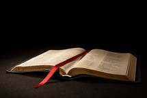Beautiful open Bible with red ribbon bookmark on pages. Warm light and black background.