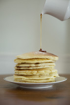 pouring syrup on a stack of pancakes 