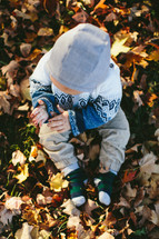 a toddler playing in fall leaves 