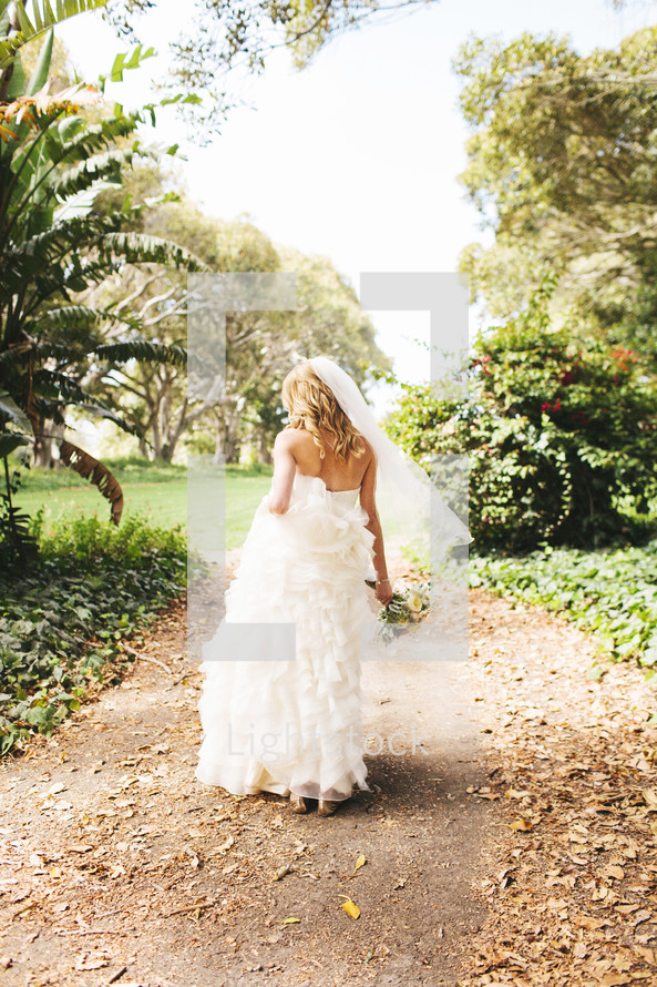 bride walking in in her bridal gown holding a bouquet along a path outdoors