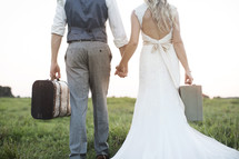 bride and groom carrying suitcases 