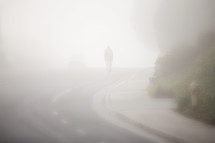 man riding a bike down a hill on a street under thick fog