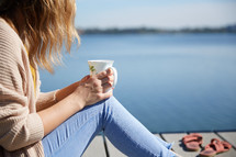 a woman sitting on a pier with a coffee cup 