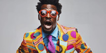 Expressive young man in colorful African attire and red glasses making a surprised face on a grey background.